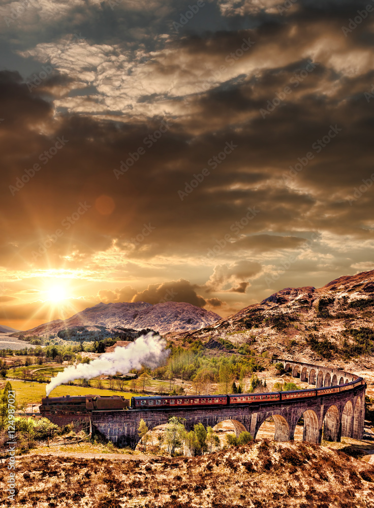 Obraz premium Glenfinnan Railway Viaduct in Scotland with the Jacobite steam train against sunset over lake