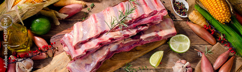 Raw beef ribs and vegetables on dark wooden background.