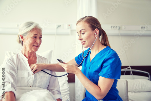 nurse with stethoscope and senior woman at clinic