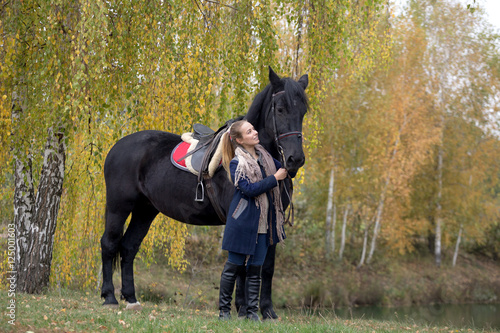 girl with a black horse in the autumn under birch