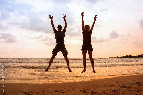 family beach holidays, happy young couple jumping at sunset