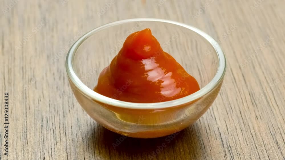 Creamy tomato ketchup dipping sauce filling up empty glass bowl against rustic wood table Creamy tomato ketchup dipping sauce filling up empty glass bowl against rustic wood table