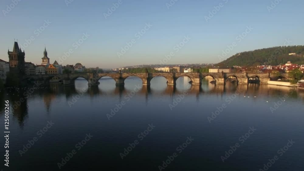 Flying over Charles bridge across Vltava river and view to riverside Prague with red rooftop architecture. Czech Republic, Europe Flying over Charles bridge across Vltava river and view to riverside Prague with red rooftop architecture. Czech Republic, Europe