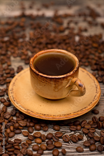 Small cup of coffee, roasted coffee beans on wooden background