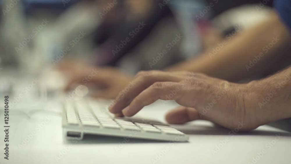 Close focus view on bearded hipster freelancer man working on his computer with mobile phone, midi controller and wireless solar keyboard on white desktop Close focus view on bearded hipster freelancer man working on his computer with mobile phone, midi controller and wireless solar keyboard on white desktop