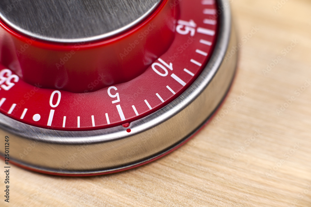 Macro view of a red kitchen timer showing 5 minutes on wooden ba Macro view of a red kitchen timer showing 5 minutes on wooden ba