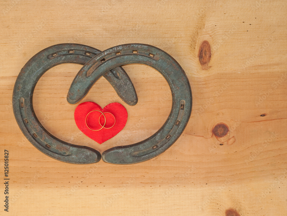 Simple Valentine design with two horseshoes forming a heart shape and two rings on rustic wood background with copy space Simple Valentine design with two horseshoes forming a heart shape and two rings on rustic wood background with copy space