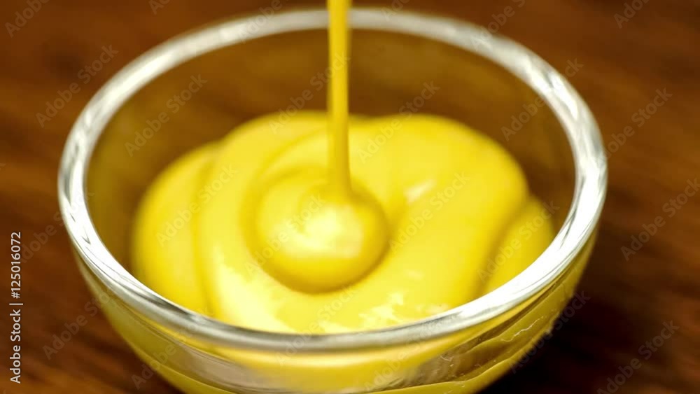 Macro of yellow colored mustard sauce condiment drizzling into glass bowl Macro of yellow colored mustard sauce condiment drizzling into glass bowl