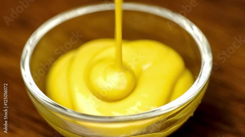 Macro of yellow colored mustard sauce condiment drizzling into glass bowl