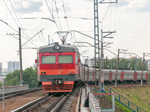 Red and grey suburban electric train moves towards on railroad turn vanishing against skyline background. Moscow, Russia. 