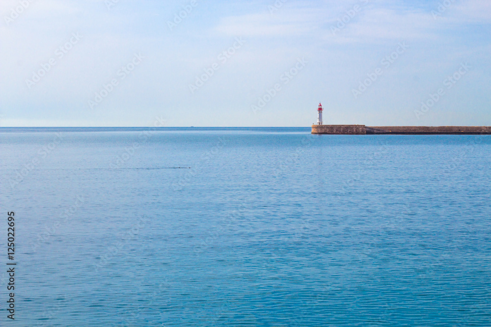 Calm sea and lighthouse at the end of the promenade.