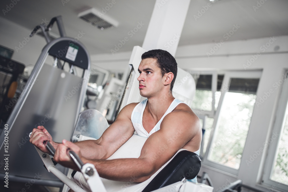 Young attractive adult man exercising and doing weight lifting at fitness gym. Sport training indoors.