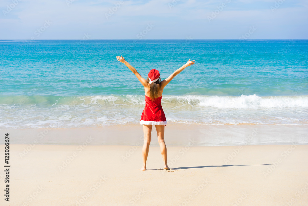 Beautiful young women in red christmas clothes with raised up hands on sea beach. New year holidays in tropical countries concept. Beautiful young women in red christmas clothes with raised up hands on sea beach. New year holidays in tropical countries concept.