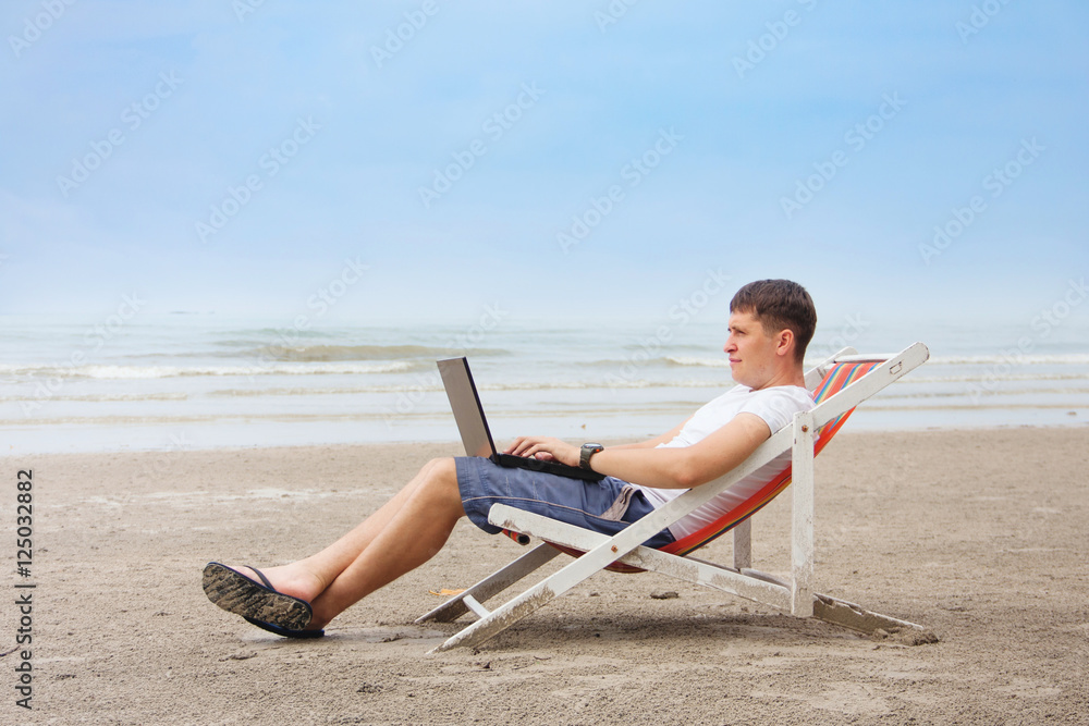 Young male freelancer working on sea beach, freelance concept