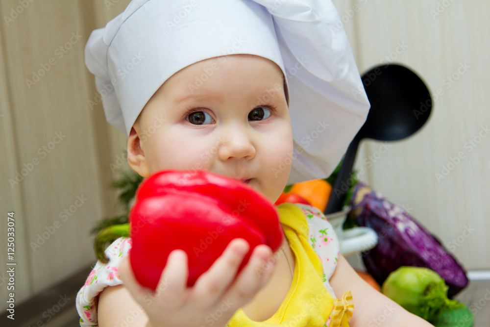 Charming little girl in a chefs hat sitting in the sink with a ladle in his hands and washes the vegetables. The concept of healthy eating and vegetarianism. Charming little girl in a chefs hat sitting in the sink with a ladle in his hands and washes the vegetables. The concept of healthy eating and vegetarianism.