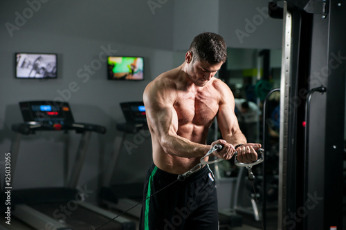 Quadro su tela Athletic strong bodybuilder deals with a dumbbell in the gym