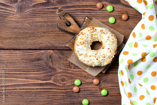 Donut with nuts and smarties on the small cutting board, wooden background, top view