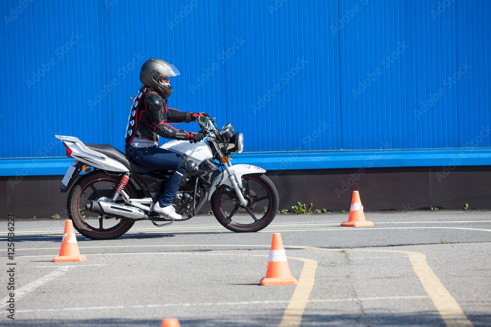 Obraz premium Kobieta kierowca robi ćwiczenie wokoło rożków na motocyklu w umiejętność trenuje motordrome. Rosyjska szkoła kierowców