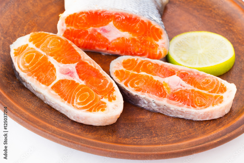 Sliced salmon and a slice of lemon on a ceramic plate.
