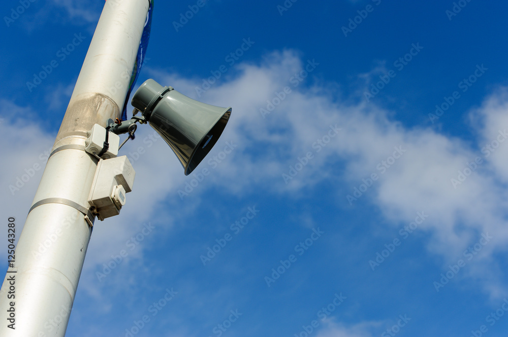 Loudspeaker on a public post against a sunny blue skye with clou Loudspeaker on a public post against a sunny blue skye with clou