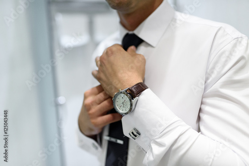 the man wears a watch and straightens his tie