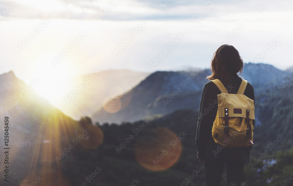 Hipster young girl with bright backpack enjoying sunset on peak of foggy mountain. Tourist traveler on background valley landscape view mockup. Hiker looking sunlight flare in trip Picos de Europa