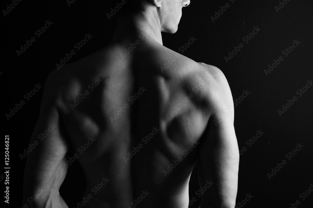 Strong muscular athletic man back on dark background, low key image, copy space