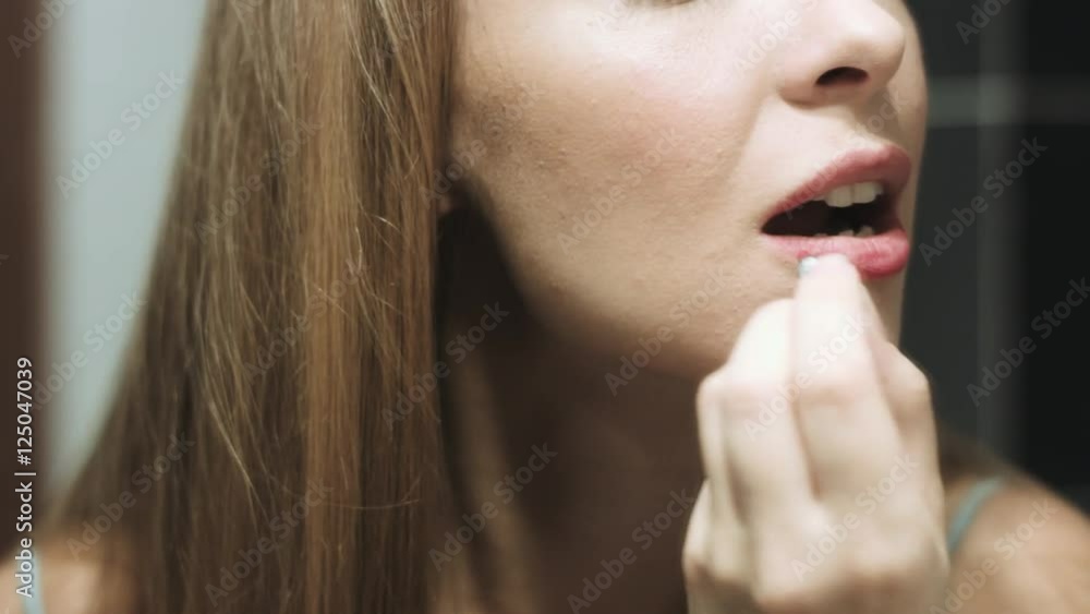 Young beautiful blond woman paints her lips bright red color lipstick in front of a mirror Young beautiful blond woman paints her lips bright red color lipstick in front of a mirror
