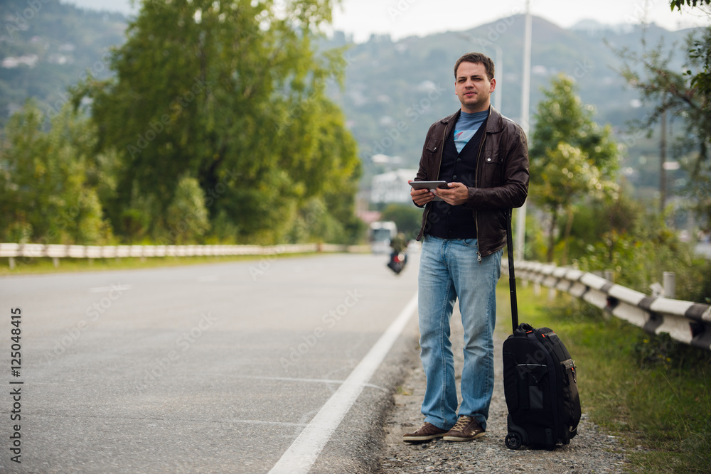 man standing with digital tablet waiting for car or taxi. Hitchhiking