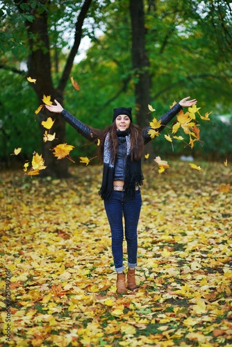 Young happy brunette woman with long hair throws maple leaves in autumn Park.