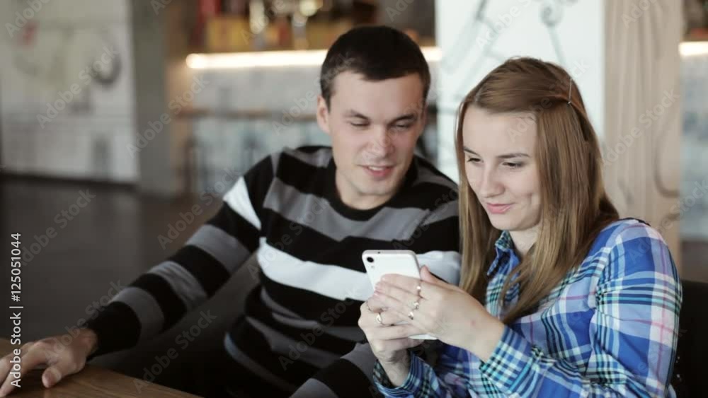 Woman and Man sitting in cafe talking and looking at phone in hand Woman and Man sitting in cafe talking and looking at phone in hand