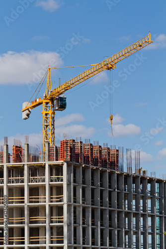 Yellow construction tower crane and house under construction