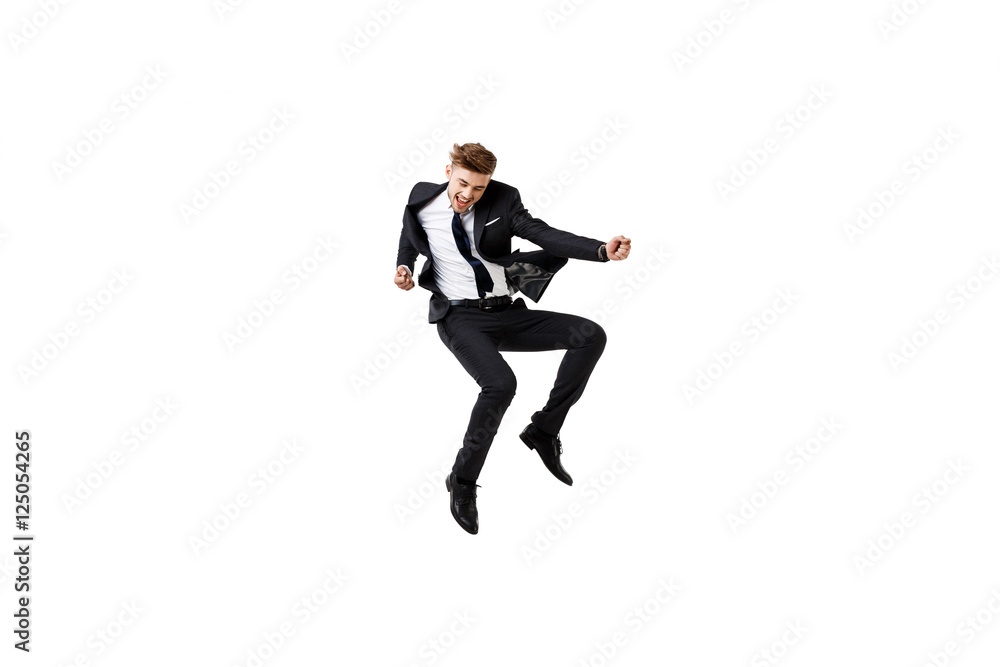 Young successful businessman in suit rejoicing, jumping over white background.