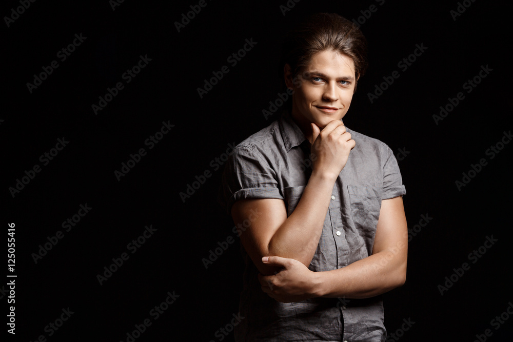 Young handsome man smiling, looking at camera over black background.