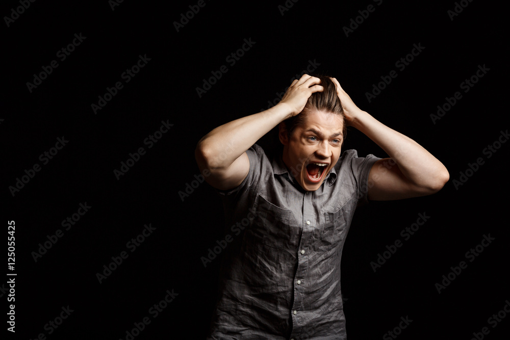Young handsome man grab his head, shouting over black background. Young handsome man grab his head, shouting over black background.