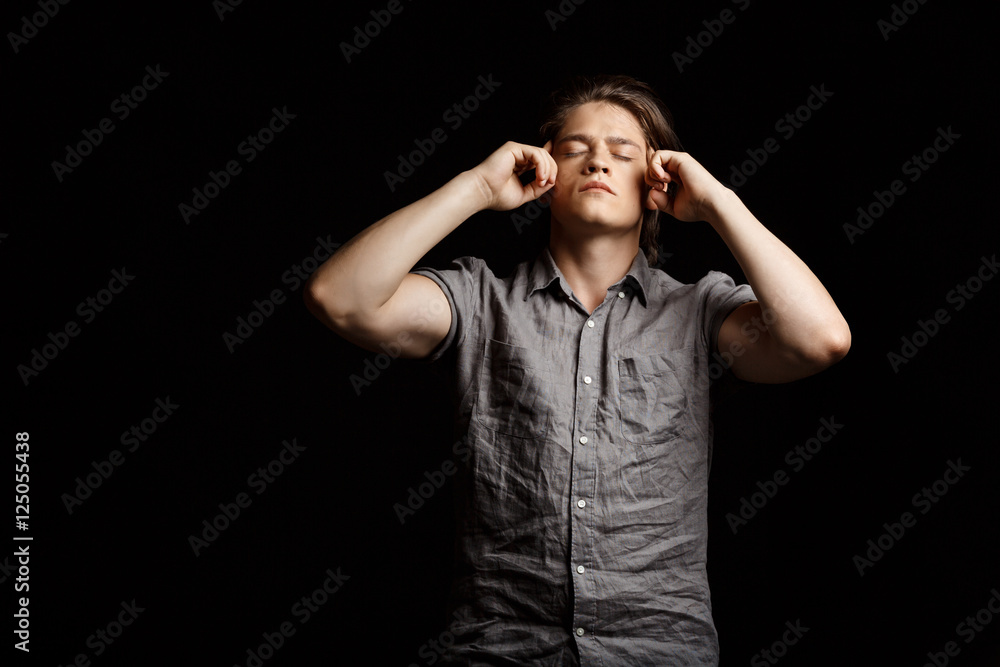Young handsome man thinking with closed eyes over black background.
