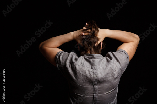 Man grab his head, standing back to camera over black background.