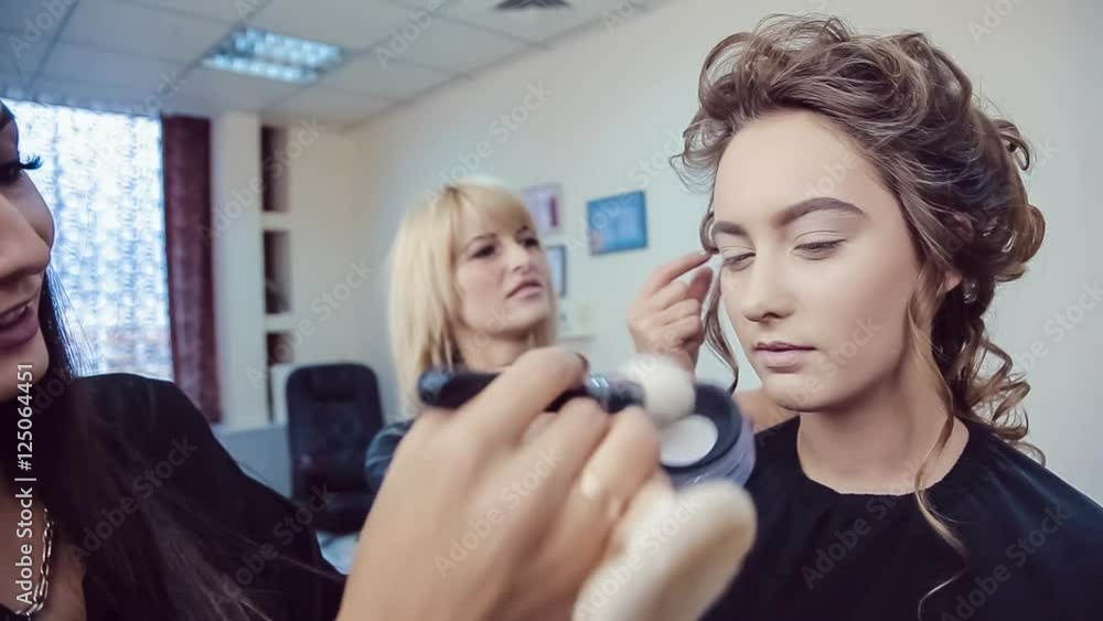 Make up artist doing professional makeup and hair stylist makes hairstyle of young woman