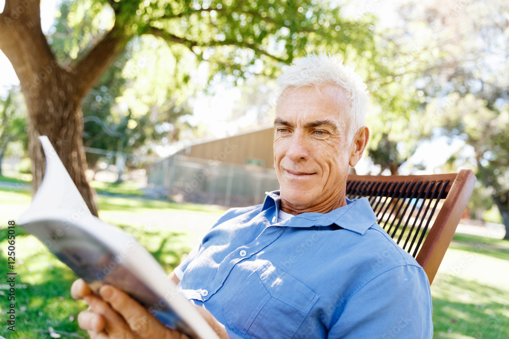 Senior man sittingin park while reading book Senior man sittingin park while reading book