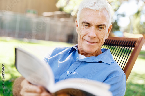 Senior man sittingin park while reading book photo