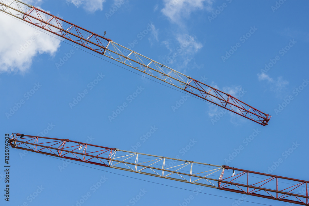 Zwei rot weiße Baukräne vor blauem Himmel und weißen Wolken
