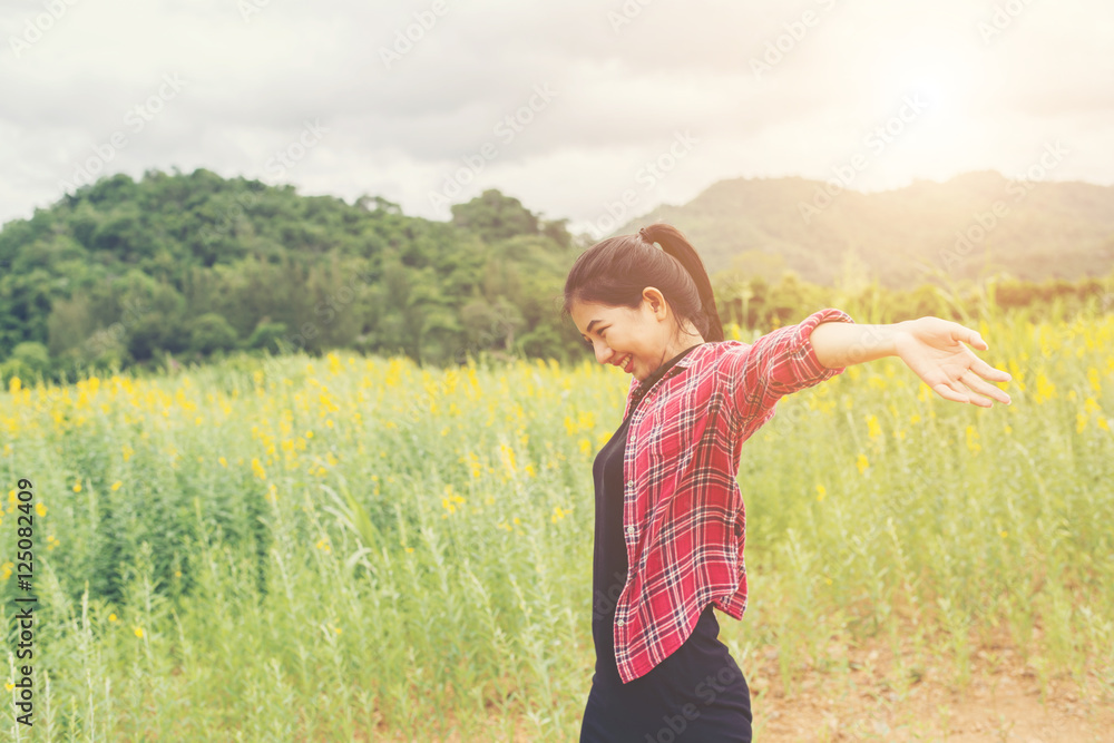 Young happy woman raising hands in yellow flower field on sunset