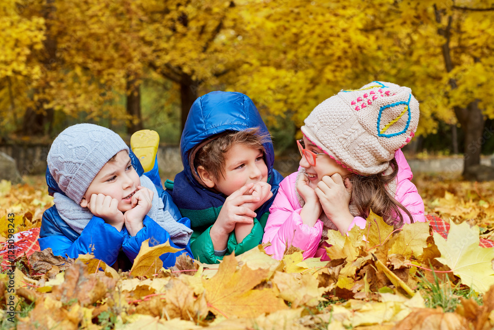 Group of children lying in a park on yellow leaves in autumn par Group of children lying in a park on yellow leaves in autumn par