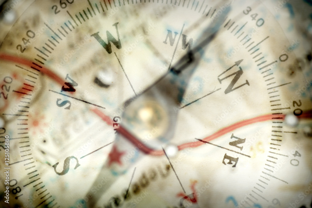 Detail of a magnetic compass on the background of the blurred image of the geographical map Detail of a magnetic compass on the background of the blurred image of the geographical map