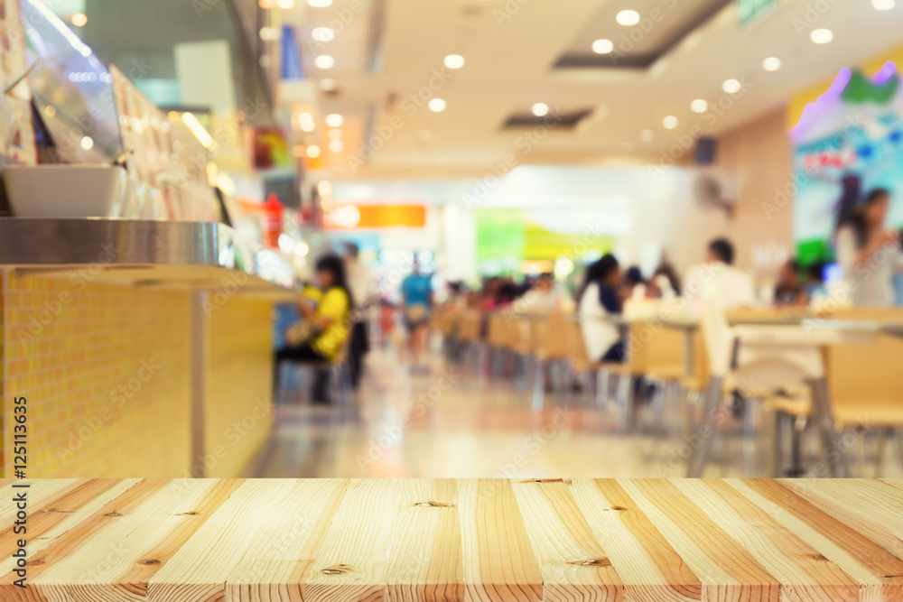 Defocused or blurred photo of food court montage with wood table top use for background.