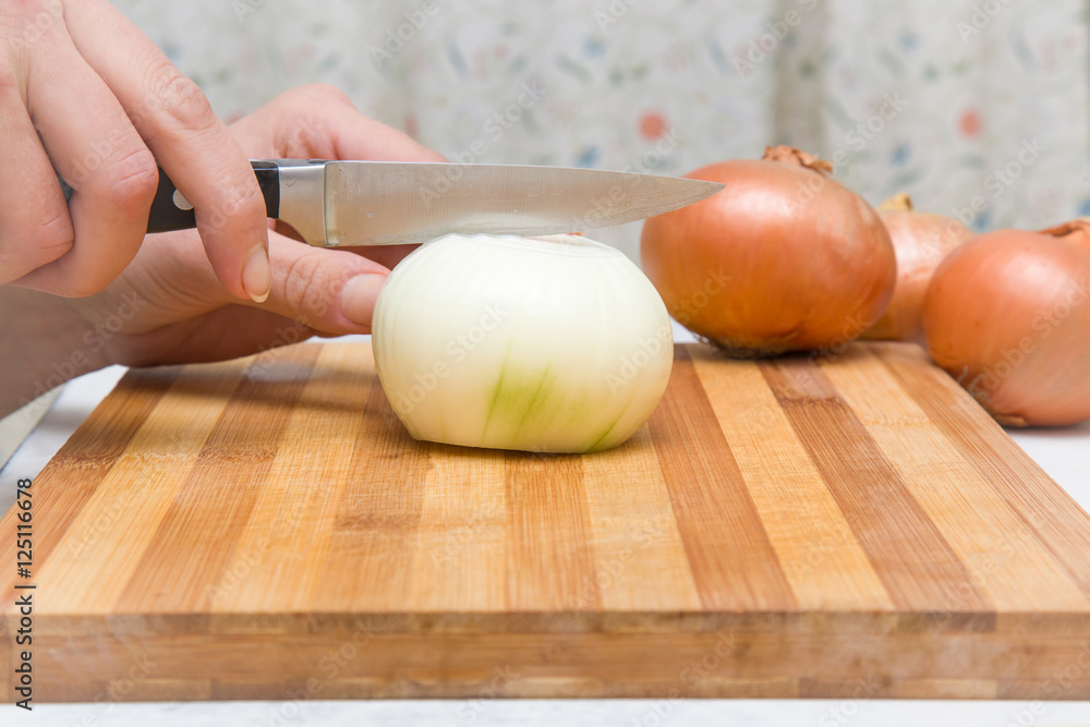 Woman's hand with a knife cuts the onion on the wooden board in the kitchen. Healthy eating and lifestyle. Woman's hand with a knife cuts the onion on the wooden board in the kitchen. Healthy eating and lifestyle.