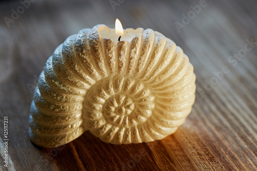 Candle in the shape of a shell burning. On wooden surface