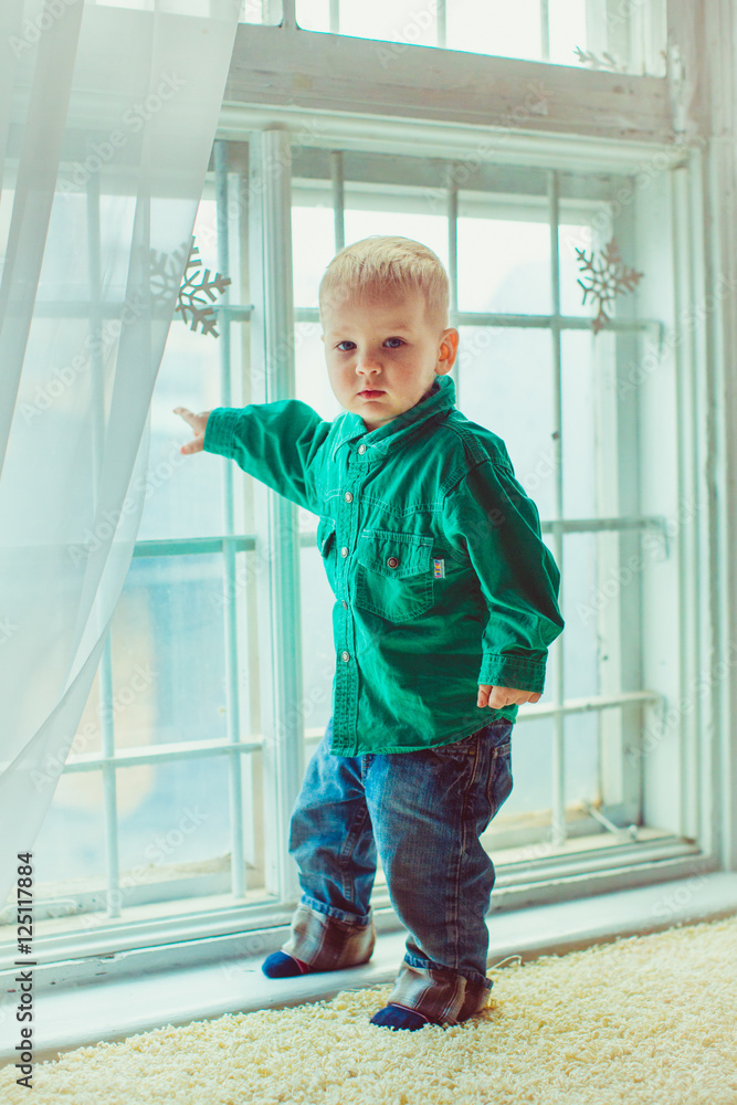 Charming boy in green shirt stands before a window decorated wit Charming boy in green shirt stands before a window decorated wit