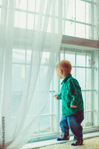 Boy in jeans and green shirt looks through the white window