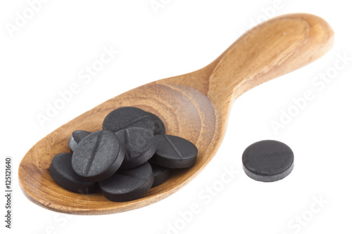 Active black charcoal pills on woodne spoon isolated on white background photo